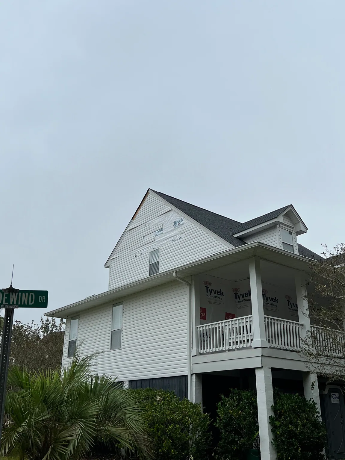 White coastal home with wind-damaged siding and exposed weather barrier